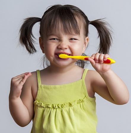 Toddler brushing teeth using a yellow toothbrush.