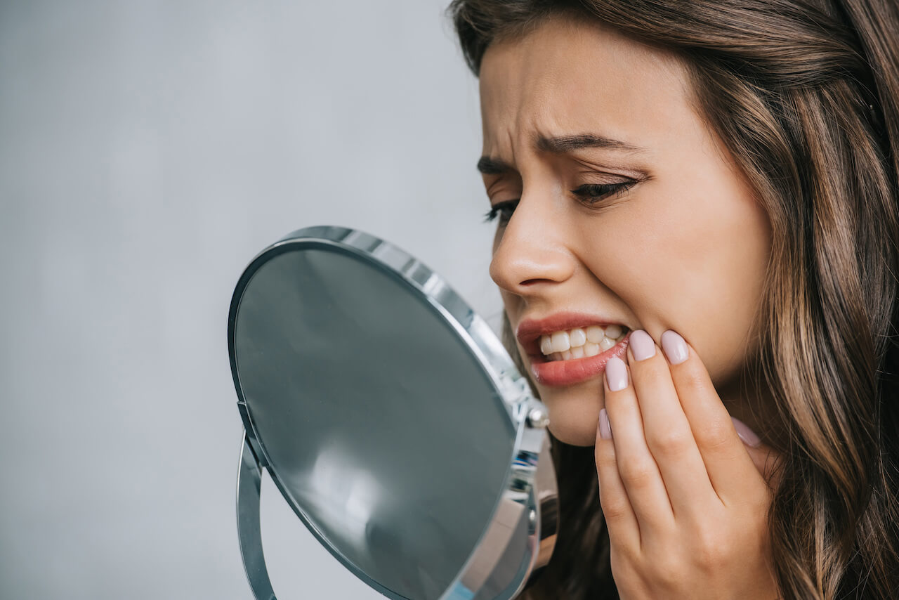 Woman checking tooth discoloration on mirror.
