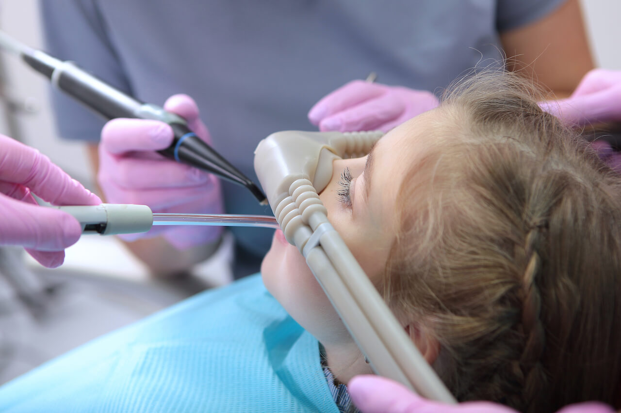 Child receiving nitrous oxide gas through a mask during dental procedure.