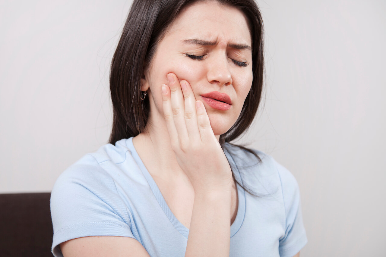 Woman experiencing intense toothache, holding her jaw in discomfort.