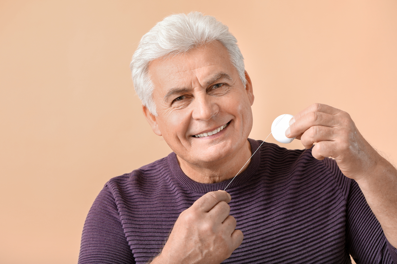 An elderly man about to floss his teeth, showcasing good oral hygiene and self-care.