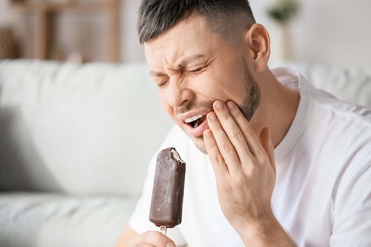 Man struggling with a sensitive teeth while eating a popsicle.